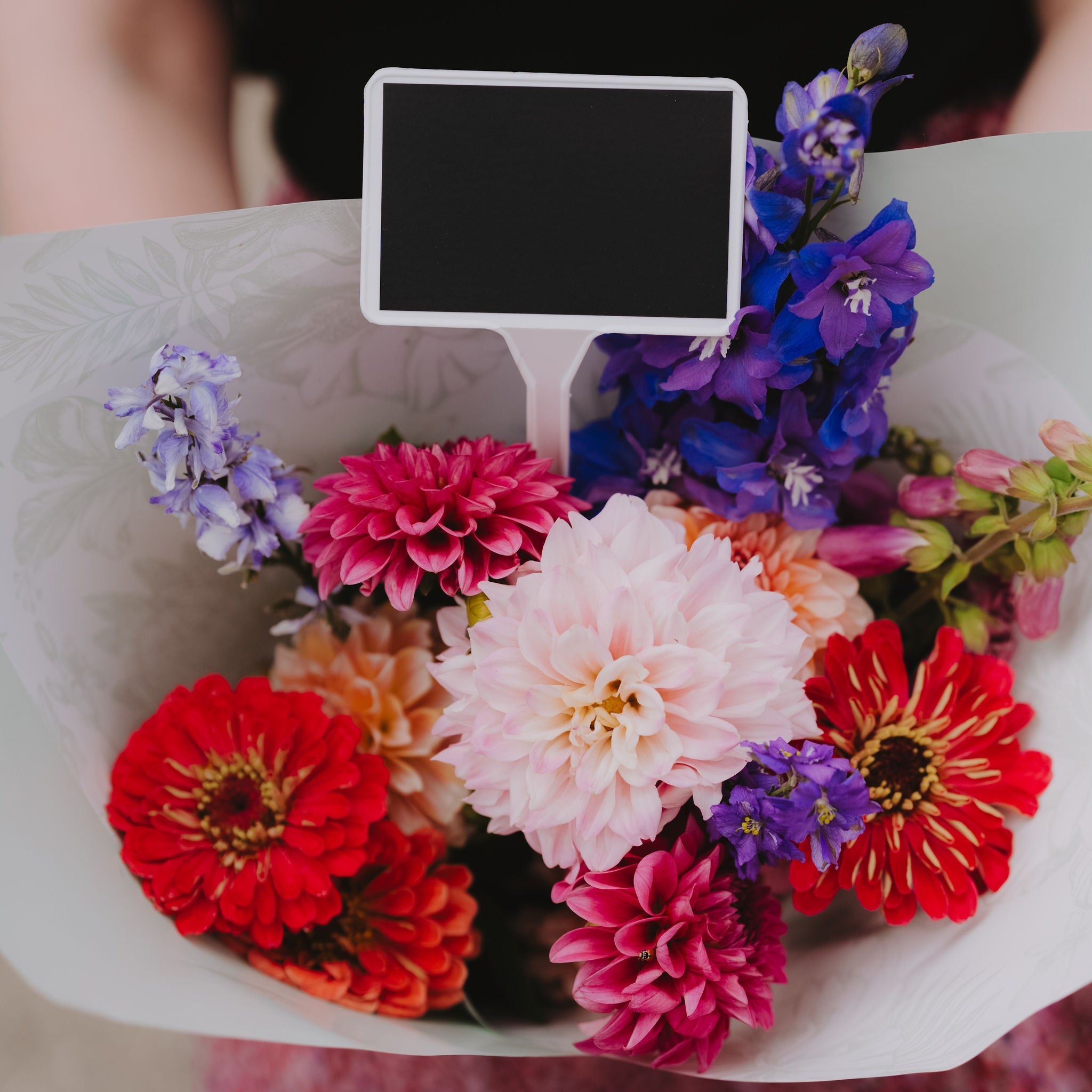 Bouquet of colorful flowers with a small blackboard in the center, held by a person.
