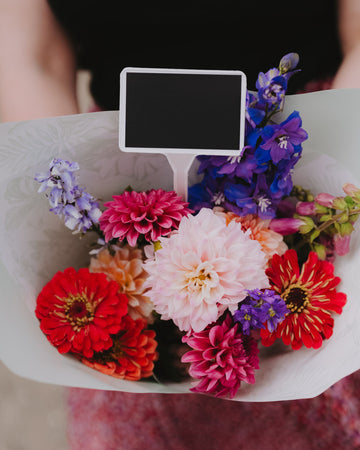 Bouquet of colorful flowers with a small blackboard in the center, held by a person.
